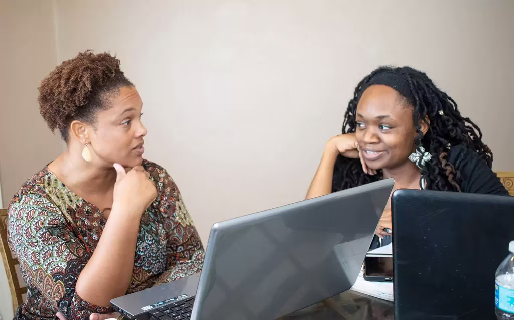 Two women talking with eachother in a meeting with computers