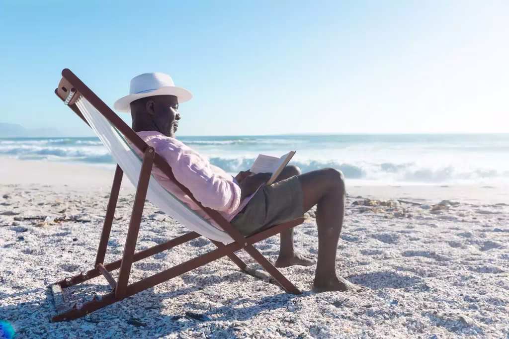 African man enjoying reading at the beach on a trip powered by QVI